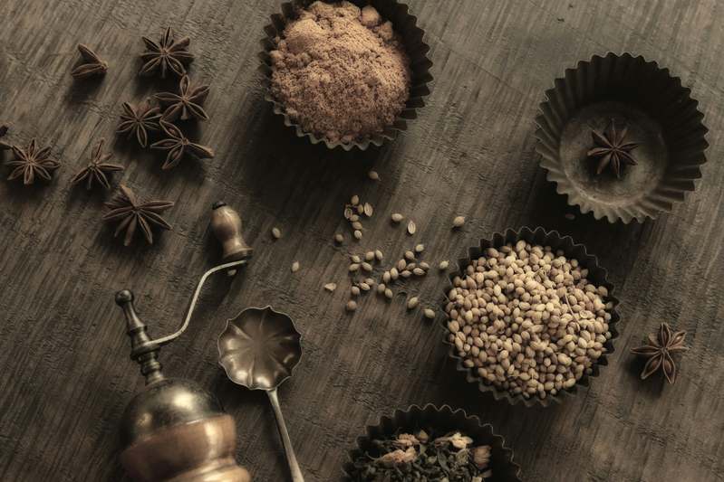 Hand holding a manual ceramic burr grinder while testing grind fineness on a white plate with visible pepper particles